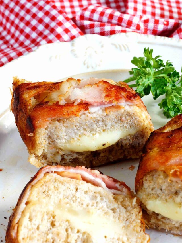 A close-up of a grilled cheese sandwich cut in half, revealing layers of melted cheese and ham, served on a white plate with a garnish of parsley.