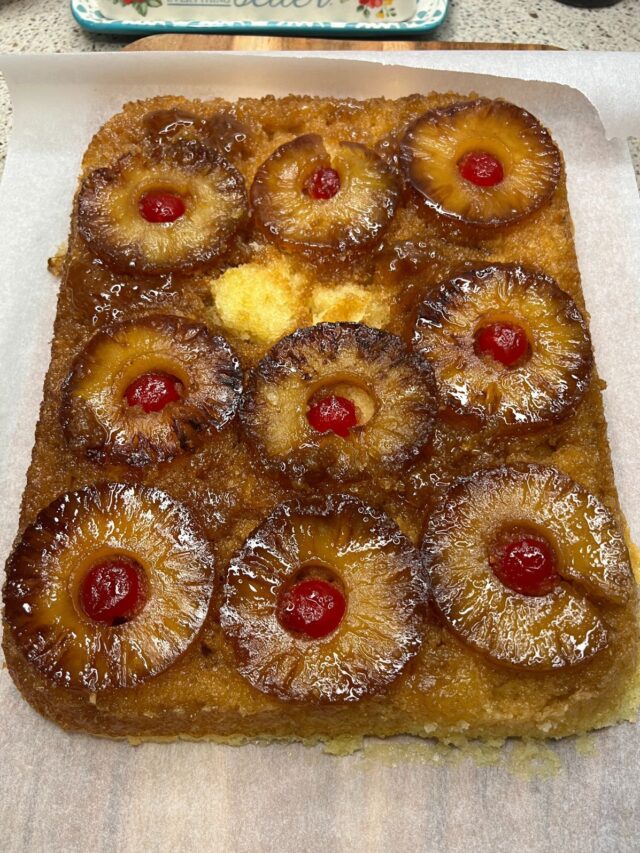 A freshly baked Blackstone pineapple upside-down cake with caramelized pineapple rings and cherries on a parchment-lined baking tray.