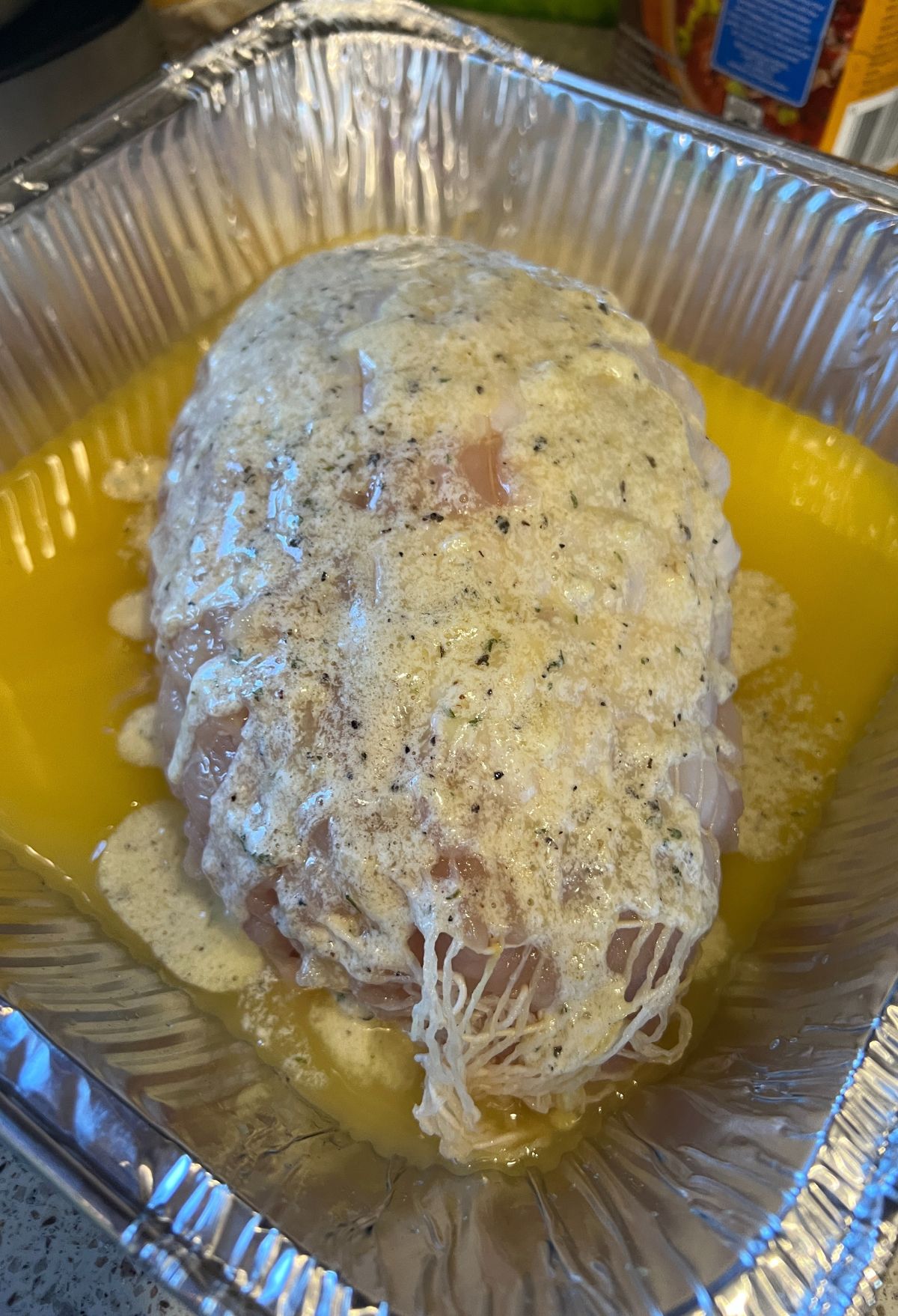 A chicken breast covered in sauce in a foil pan.