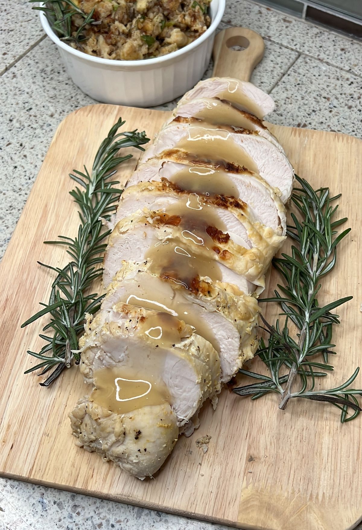 Sliced turkey with rosemary and stuffing on a cutting board.