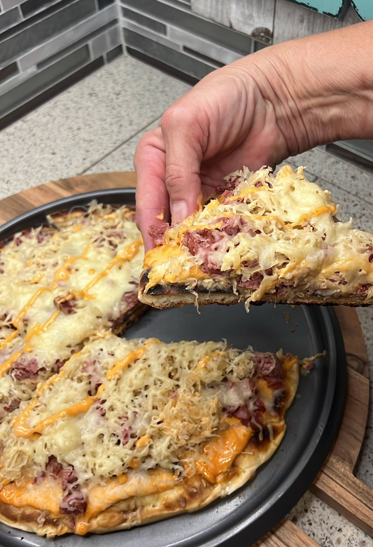 A person using a Blackstone Pizza Oven removing a slice of rueben pizza from a pan.