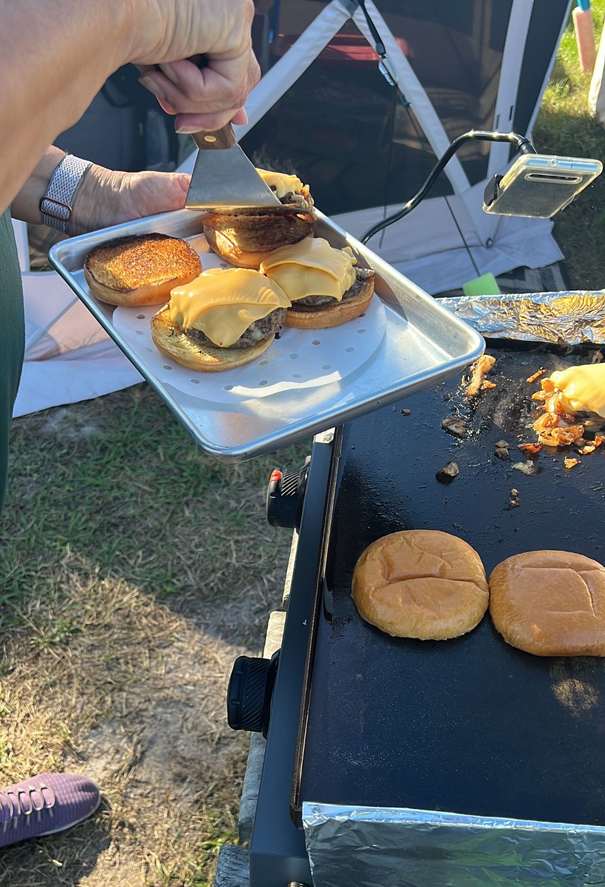 A woman is preparing hamburgers on a grill.