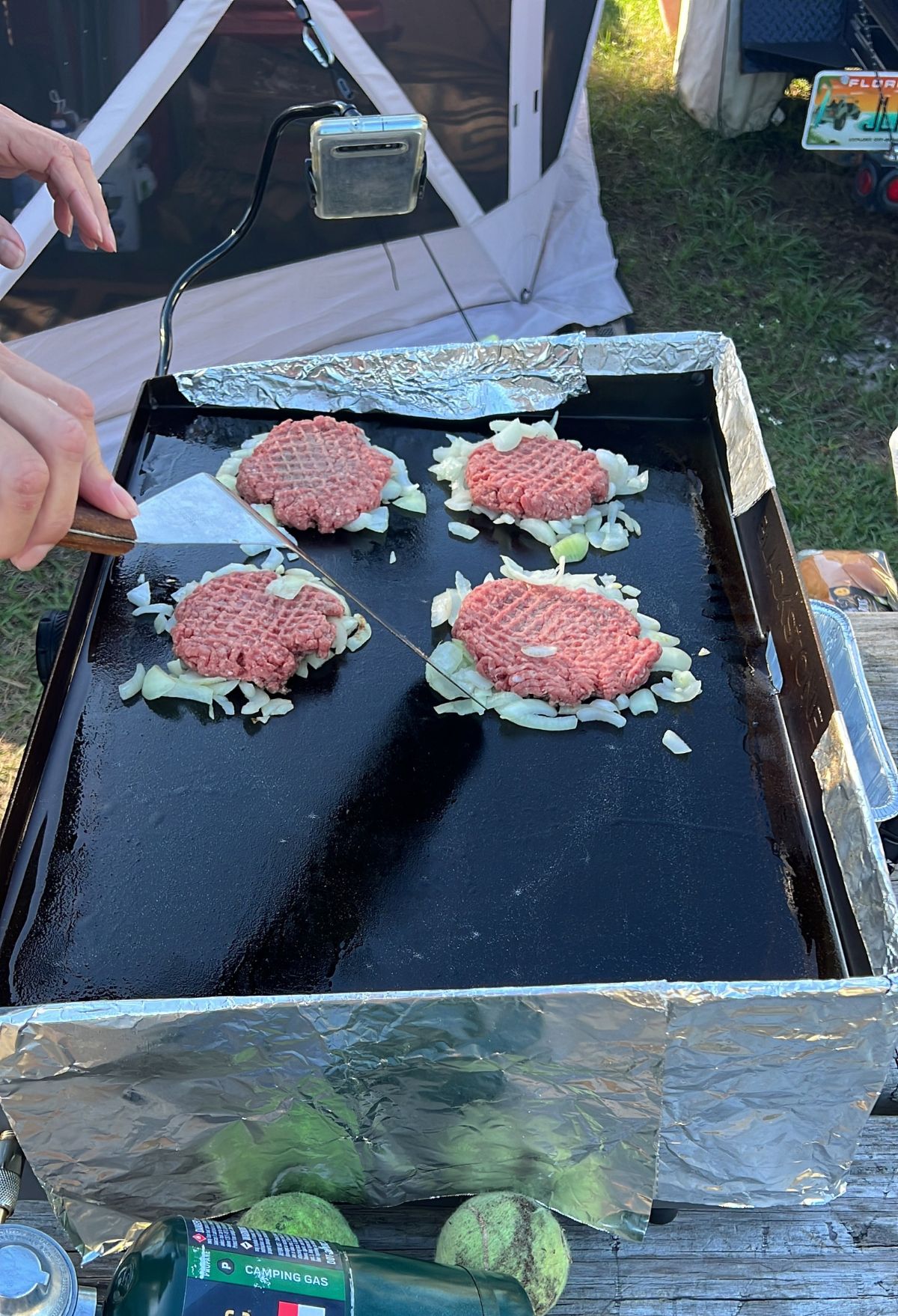 A person is preparing hamburgers on a grill.