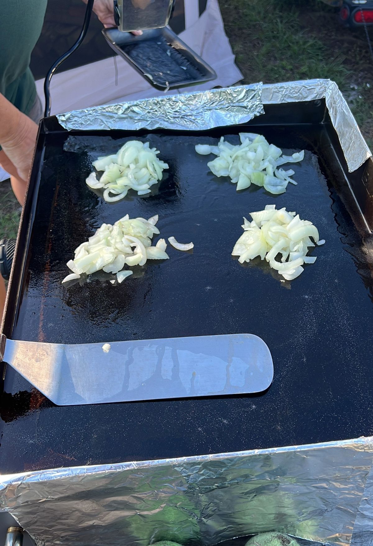 A person is putting onions on a griddle.