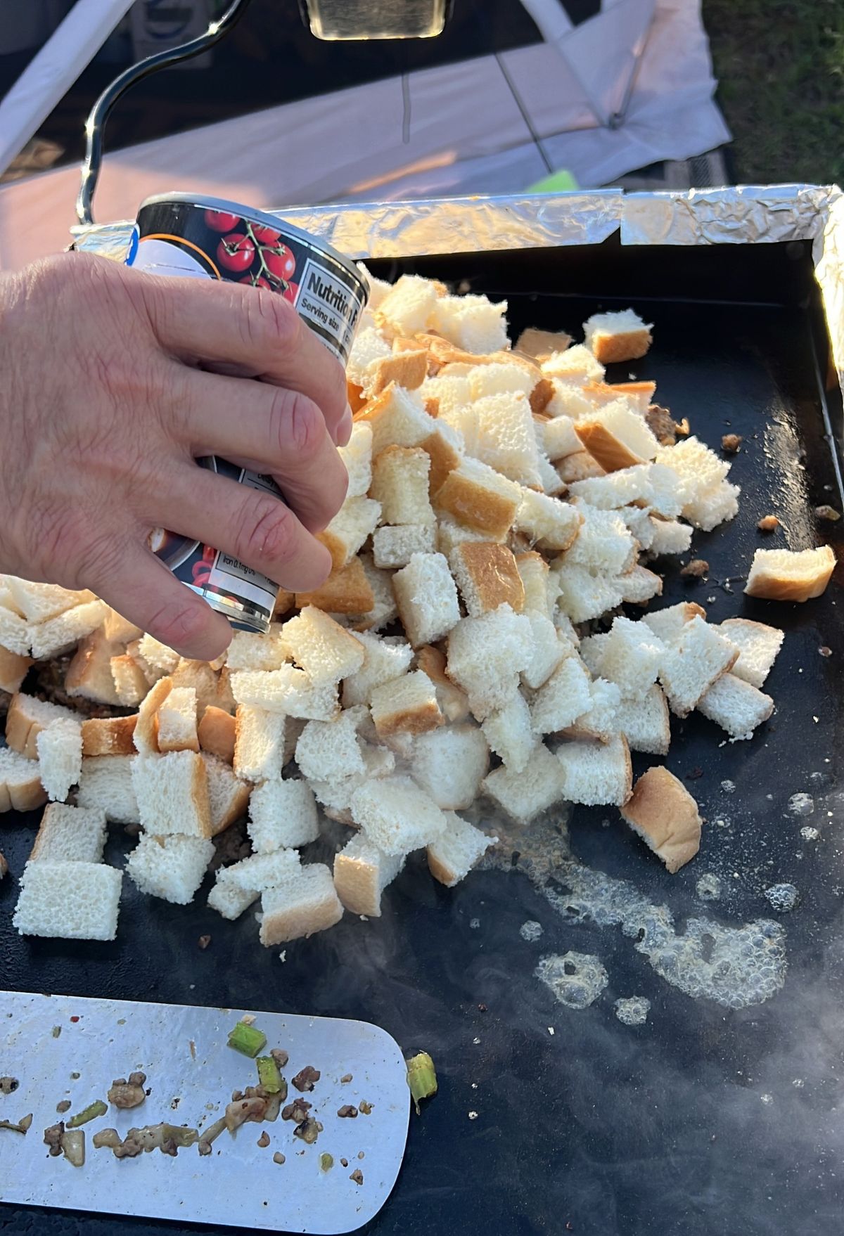 A person pouring a can onto a pan of bread cubes.