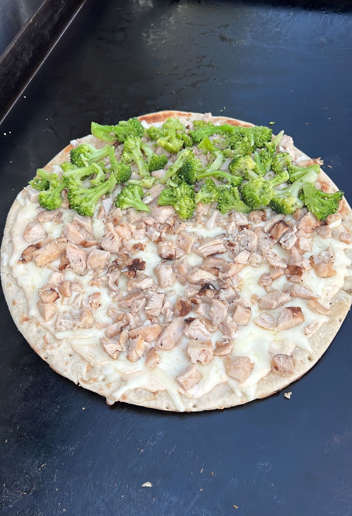A pizza with chicken and broccoli on it.