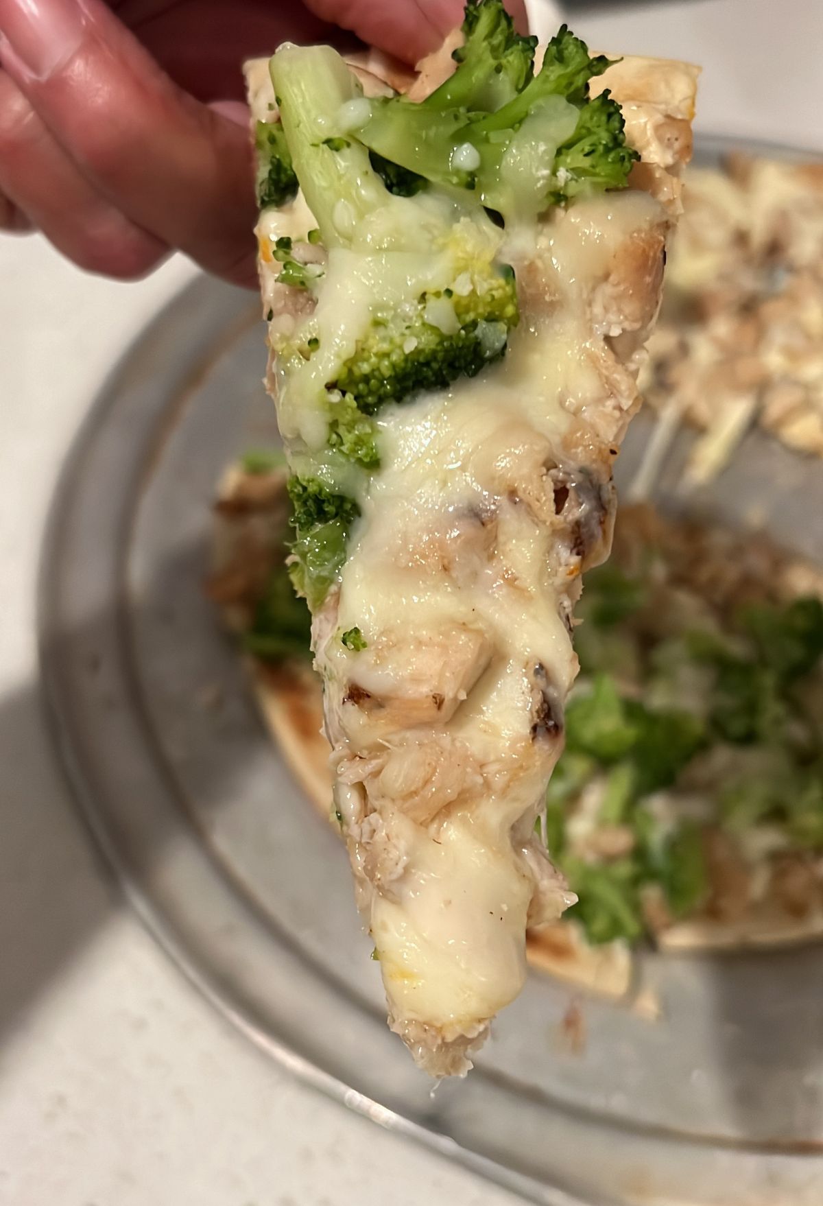 A person holding up a slice of pizza with broccoli and cheese.