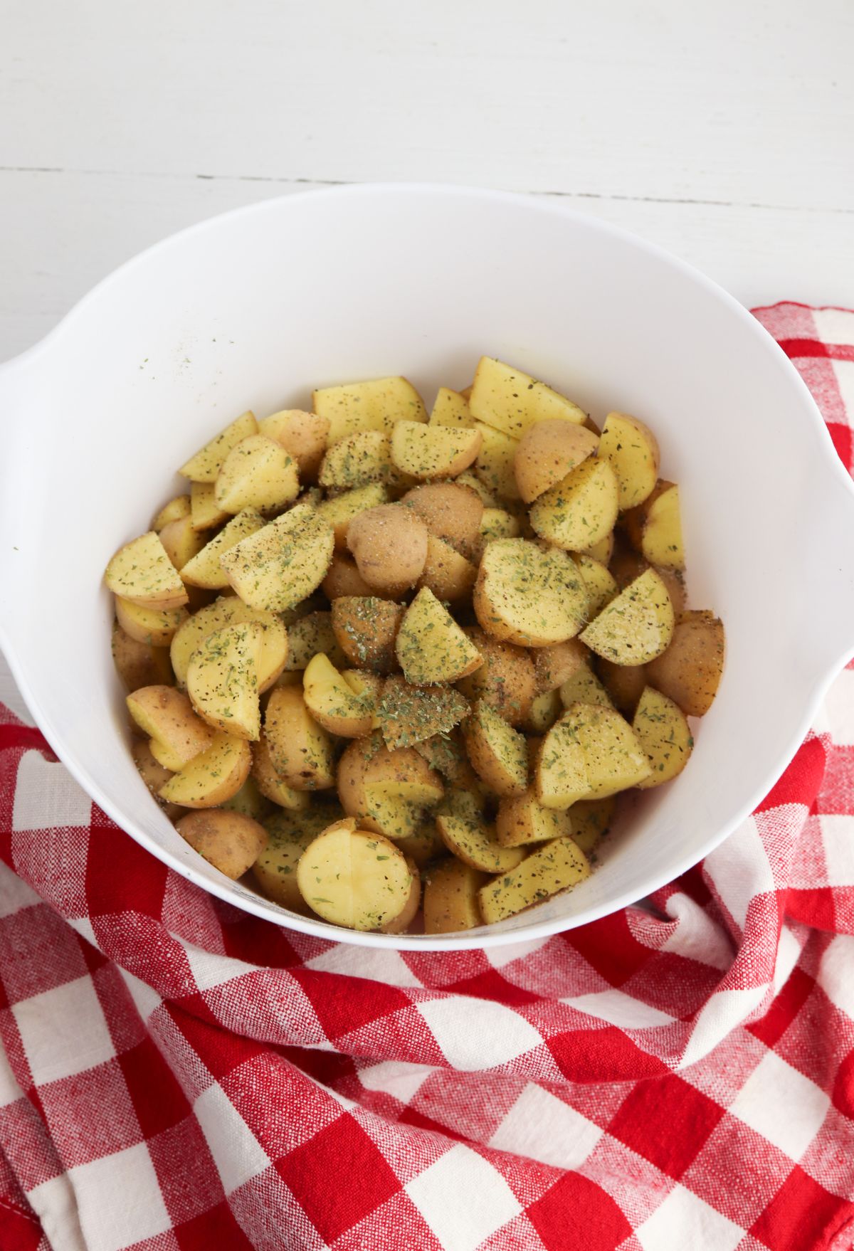 Roasted potatoes in a white bowl on a red and white checkered tablecloth.
