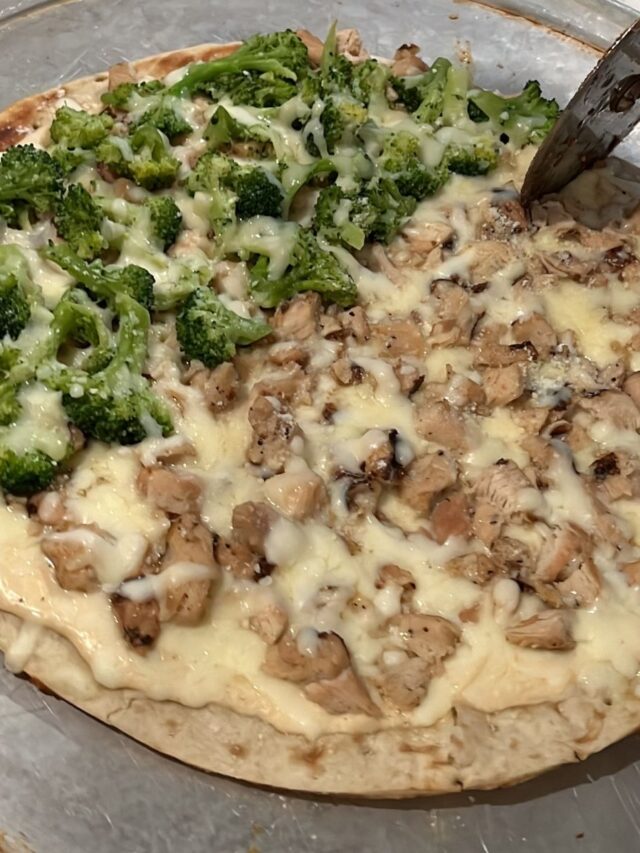 Pizza with broccoli and diced chicken topped with melted cheese, being sliced with a pizza cutter for an easy pizza recipe.