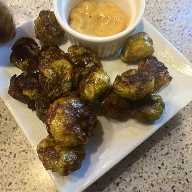 Roasted brussels sprouts on a plate with dipping sauce.