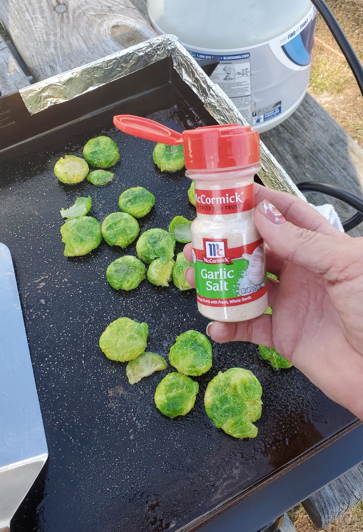 Brussel sprouts on a grill with a bottle of seasoning.