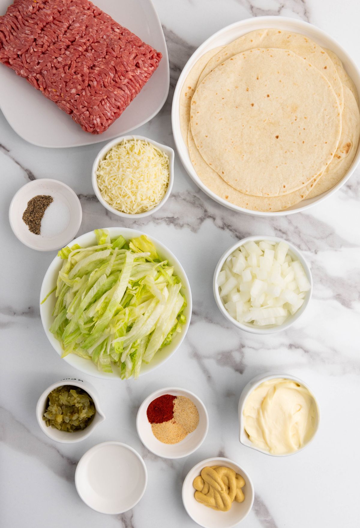Ingredients for a meat and cheese burrito on a marble table.
