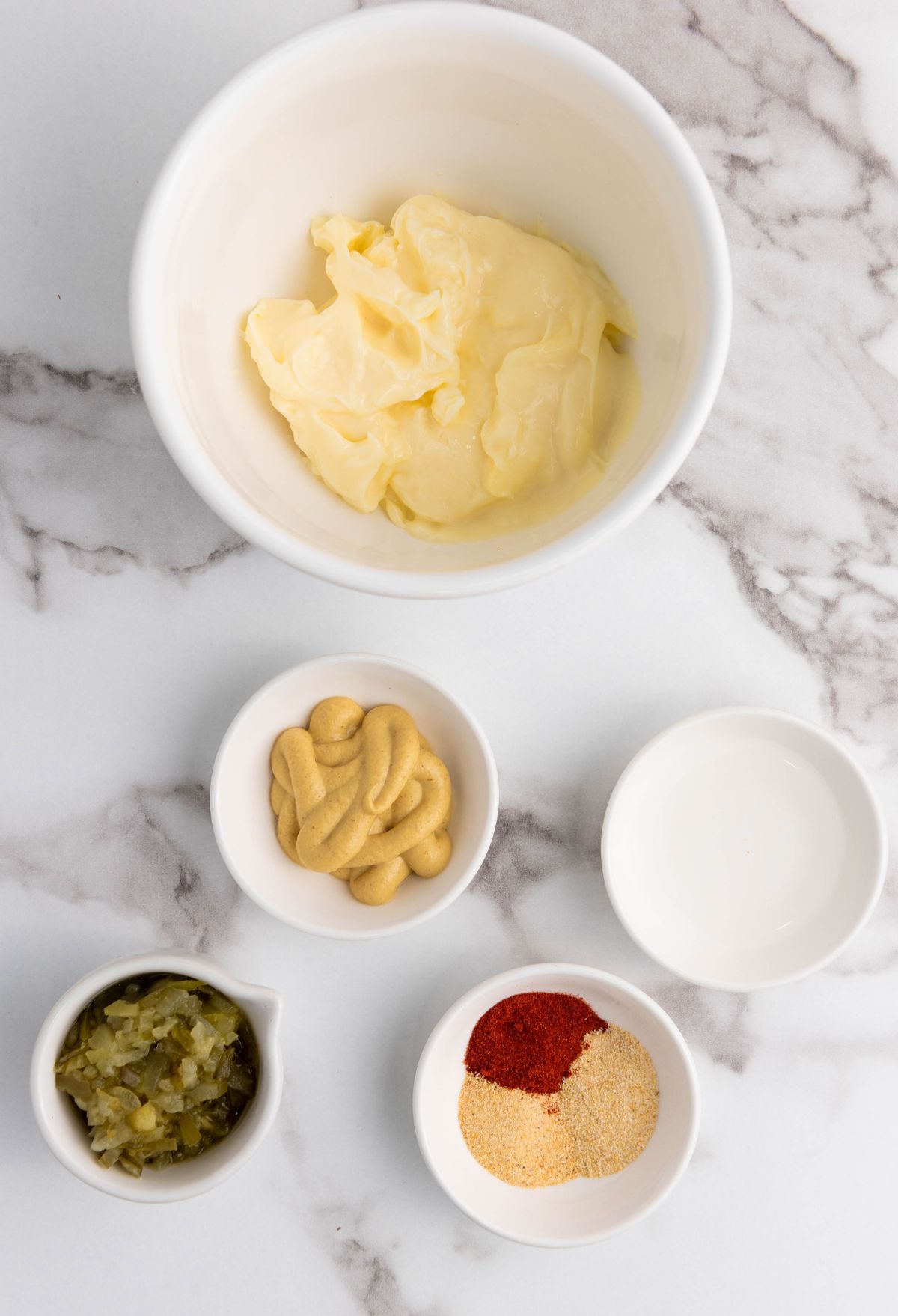 A bowl of butter, mustard, and other ingredients on a marble countertop.