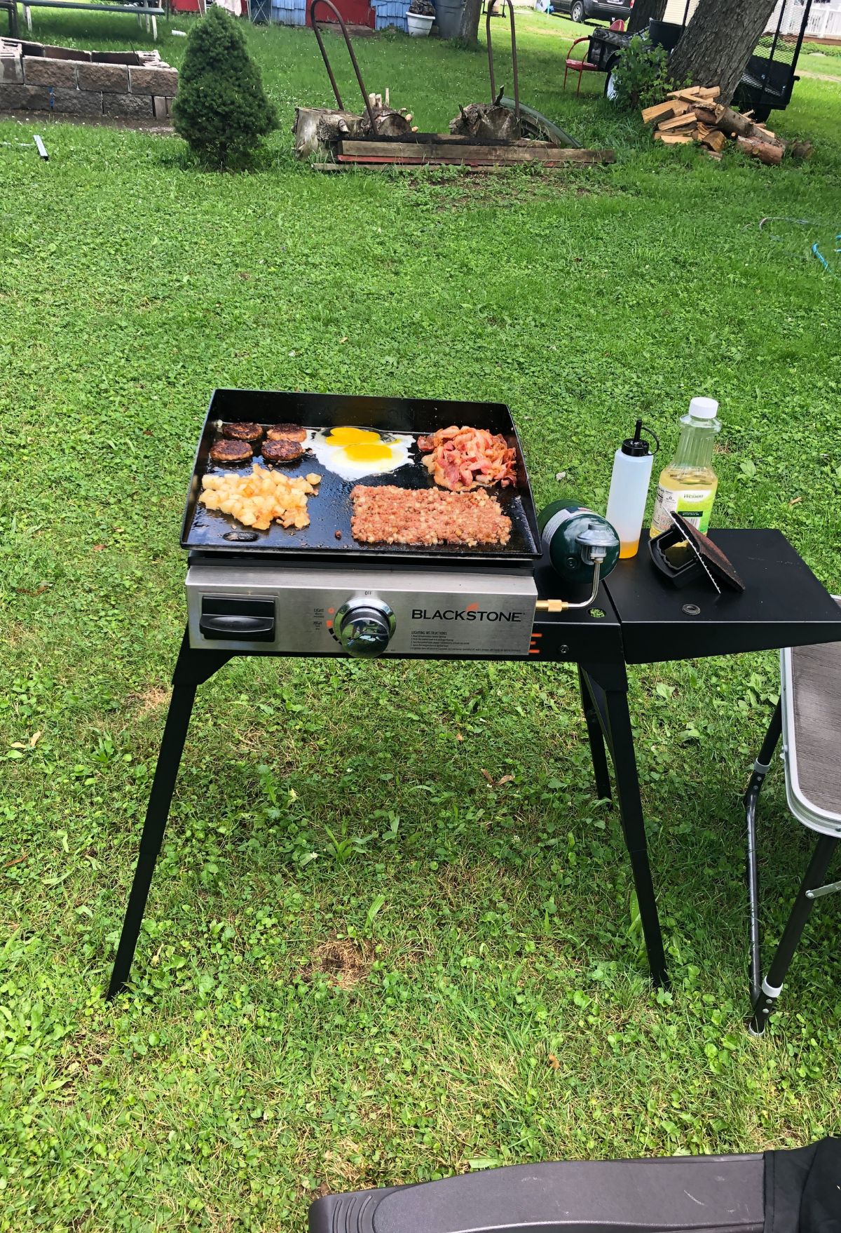 A blackstone grill in the grass with cooking food on it.