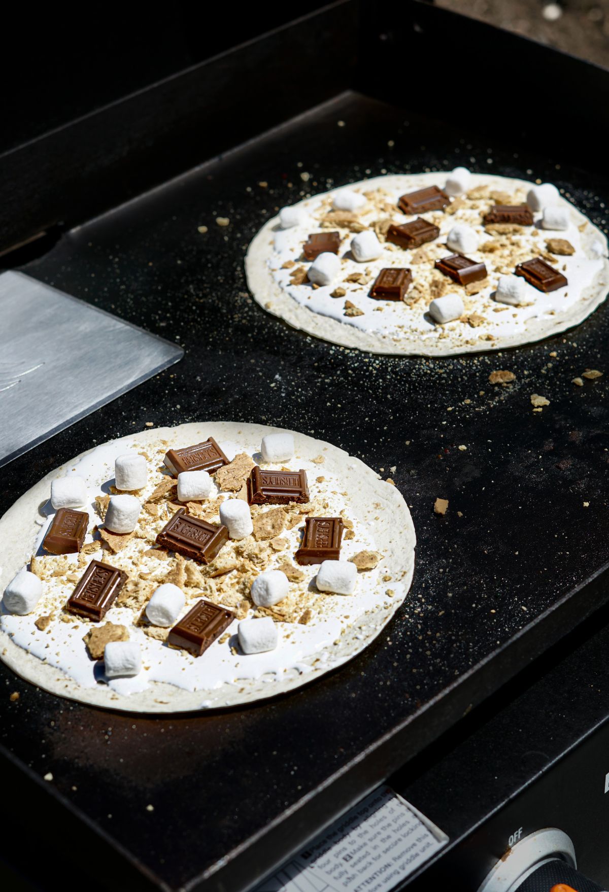 Two pizzas on a grill with marshmallows on them.