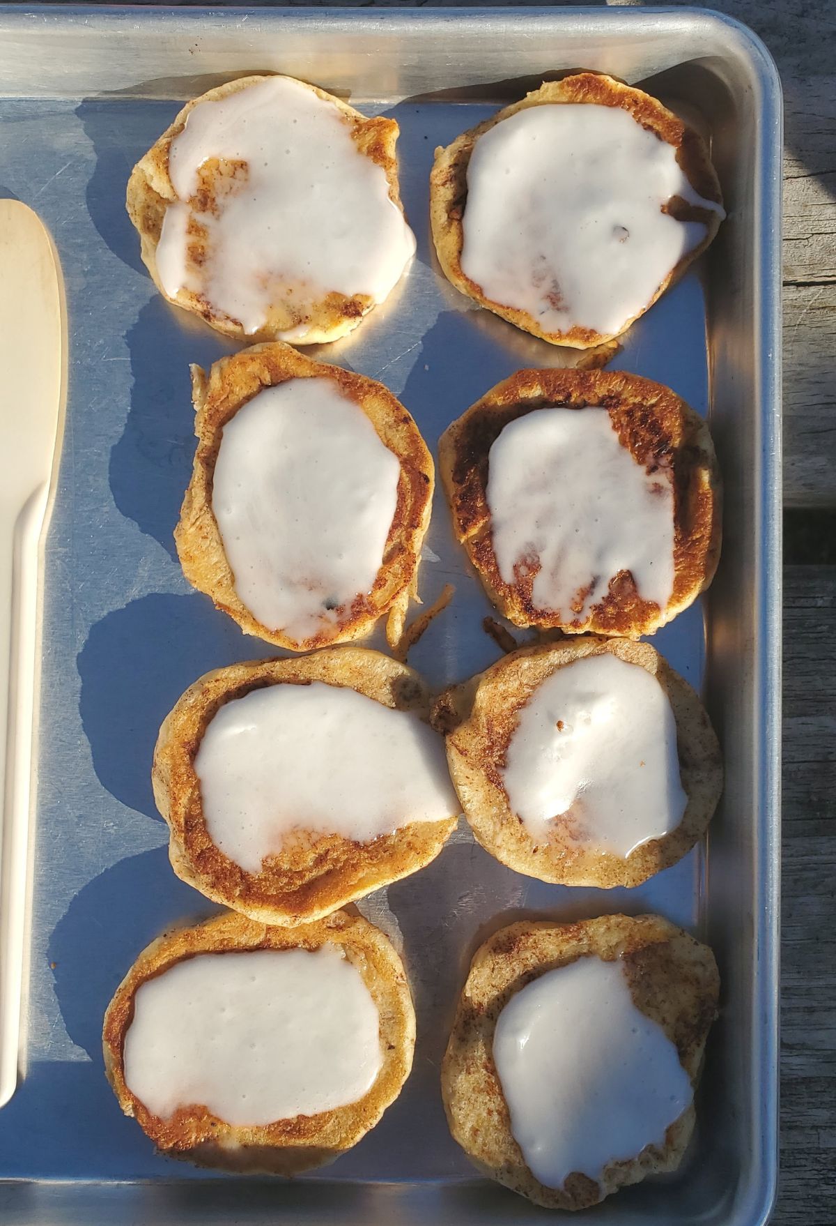 Pancakes with icing and a spoon on a metal tray.