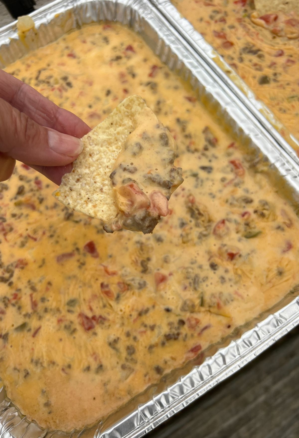 A person holding a piece of cheesy dip in a pan.