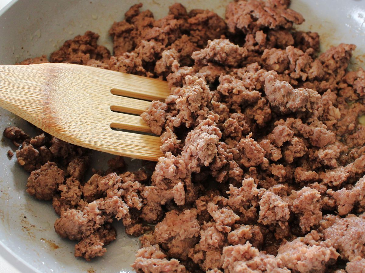 Ground beef in a pan with a wooden spoon.