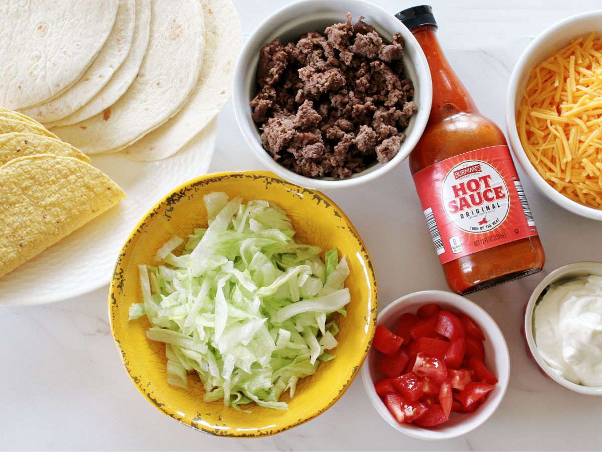 A bowl of tacos, salsa, cheese and other ingredients.