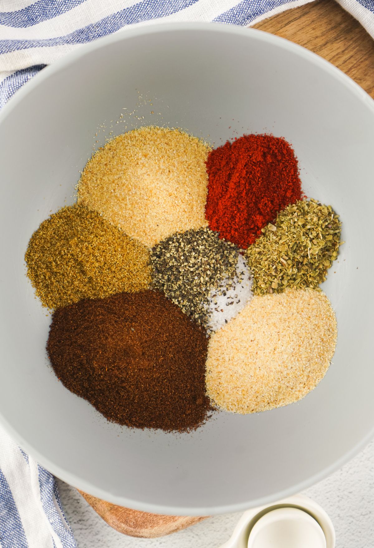 A bowl of spices and seasonings on a wooden cutting board.