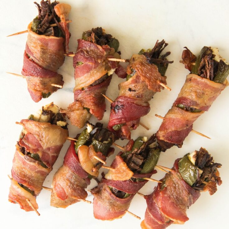 A plate of wrapped bacon and peppers with toothpicks.