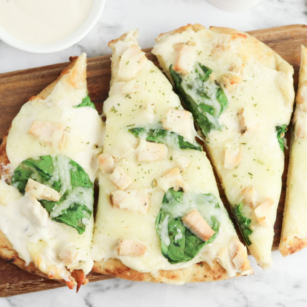 Chicken and spinach pizza on a wooden cutting board.