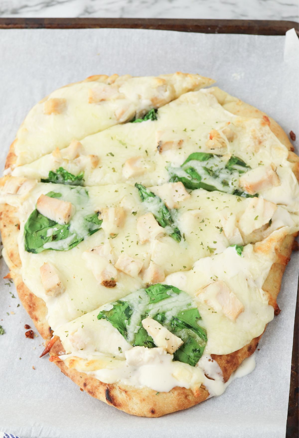 A pizza with chicken and spinach on it.