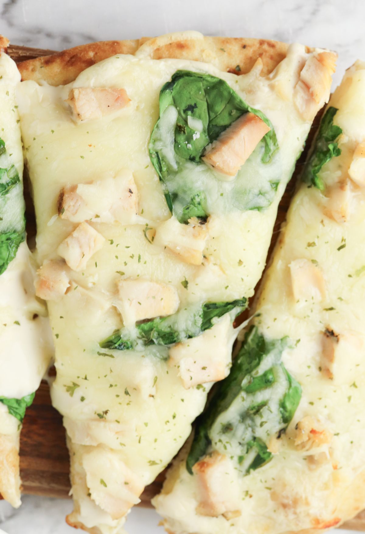 Chicken and spinach pizza on a wooden cutting board.
