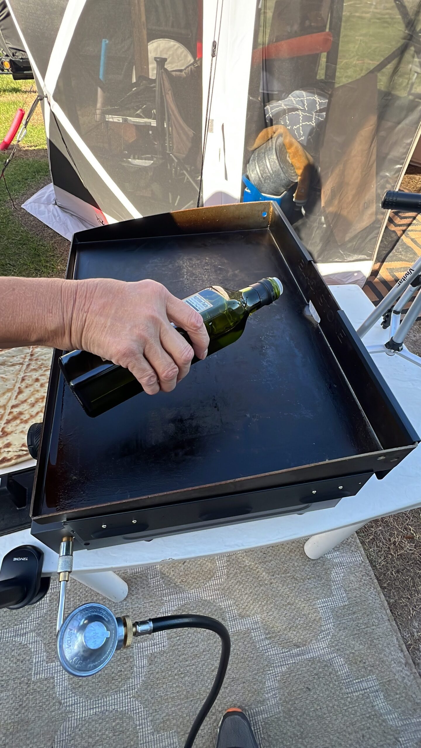 A person pouring a bottle of wine onto a grill.
