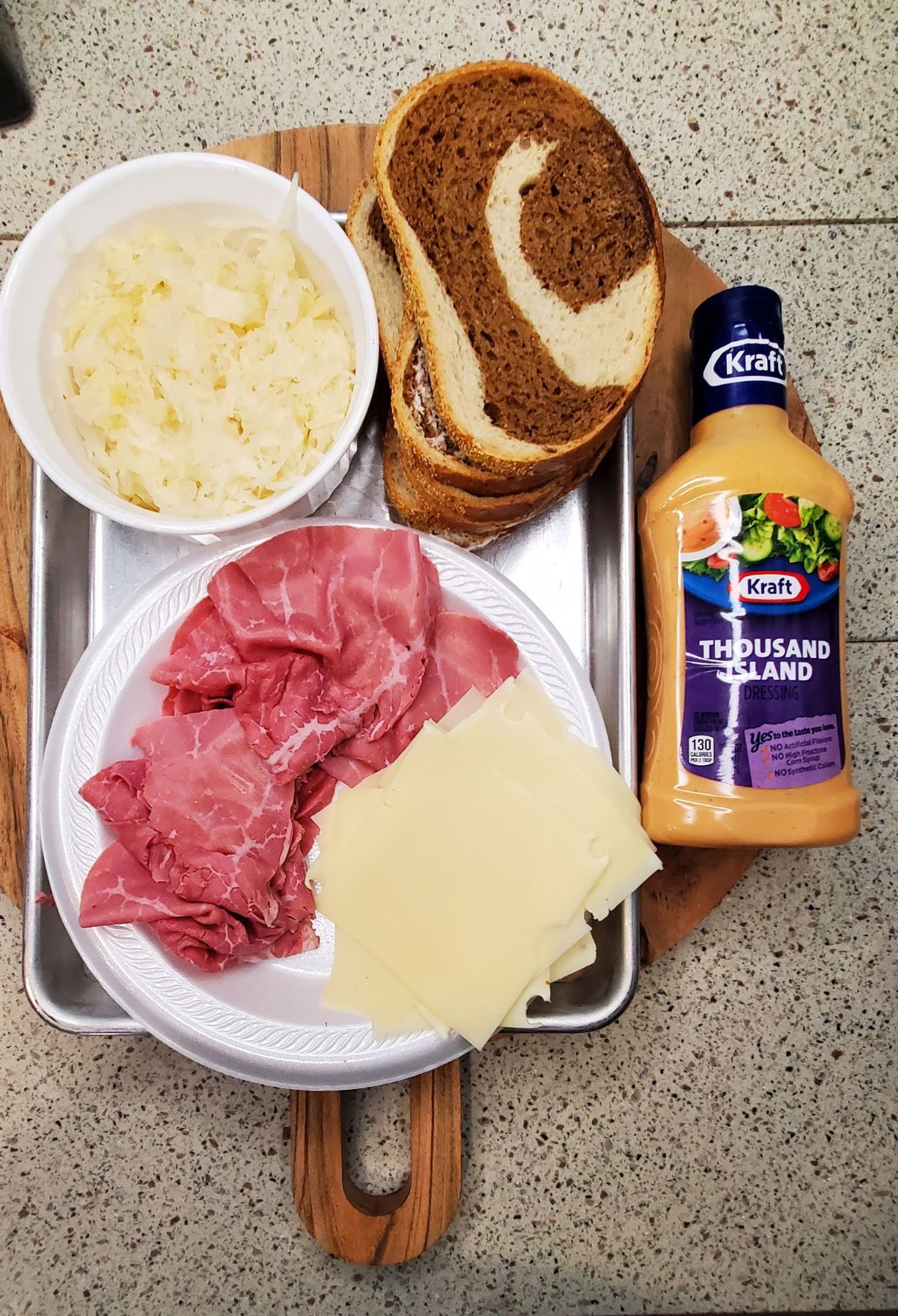 A plate with bread, meat, onions, and 1000 island dressing.