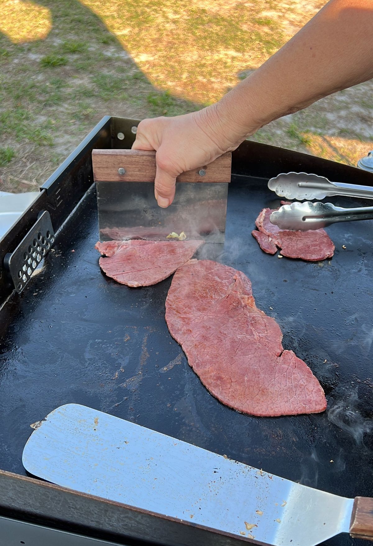 A person is slicing meat on a grill.