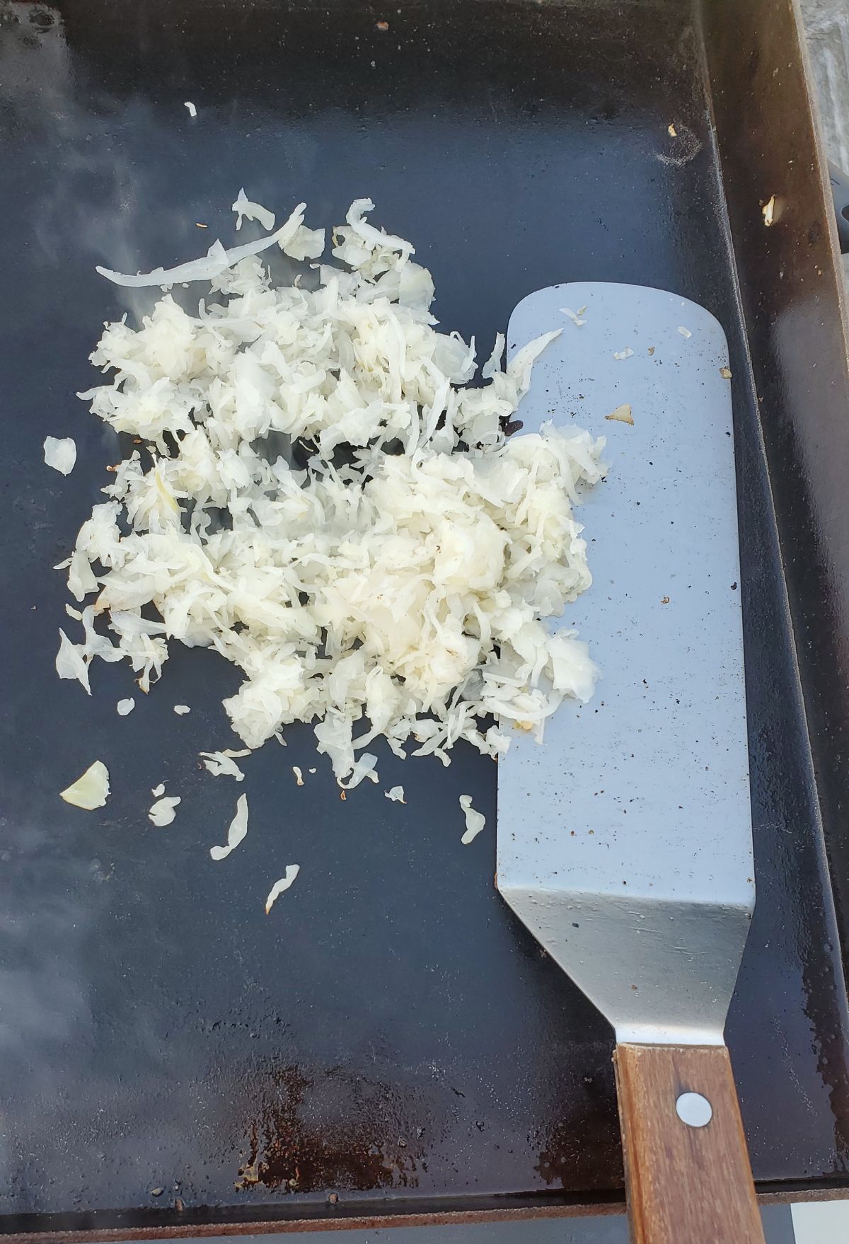 Shredded onions on a griddle with a spatula.