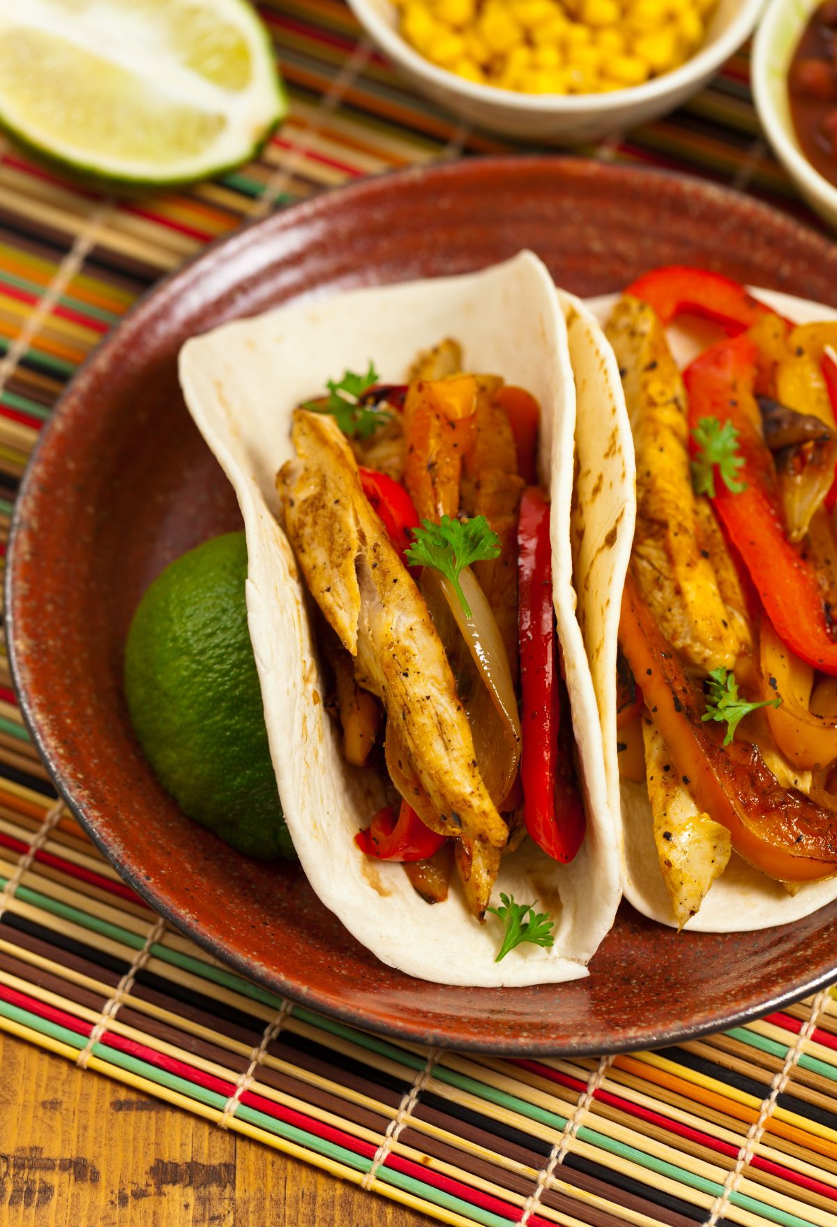 Two chicken fajitas with bell peppers and lime in a serving dish.