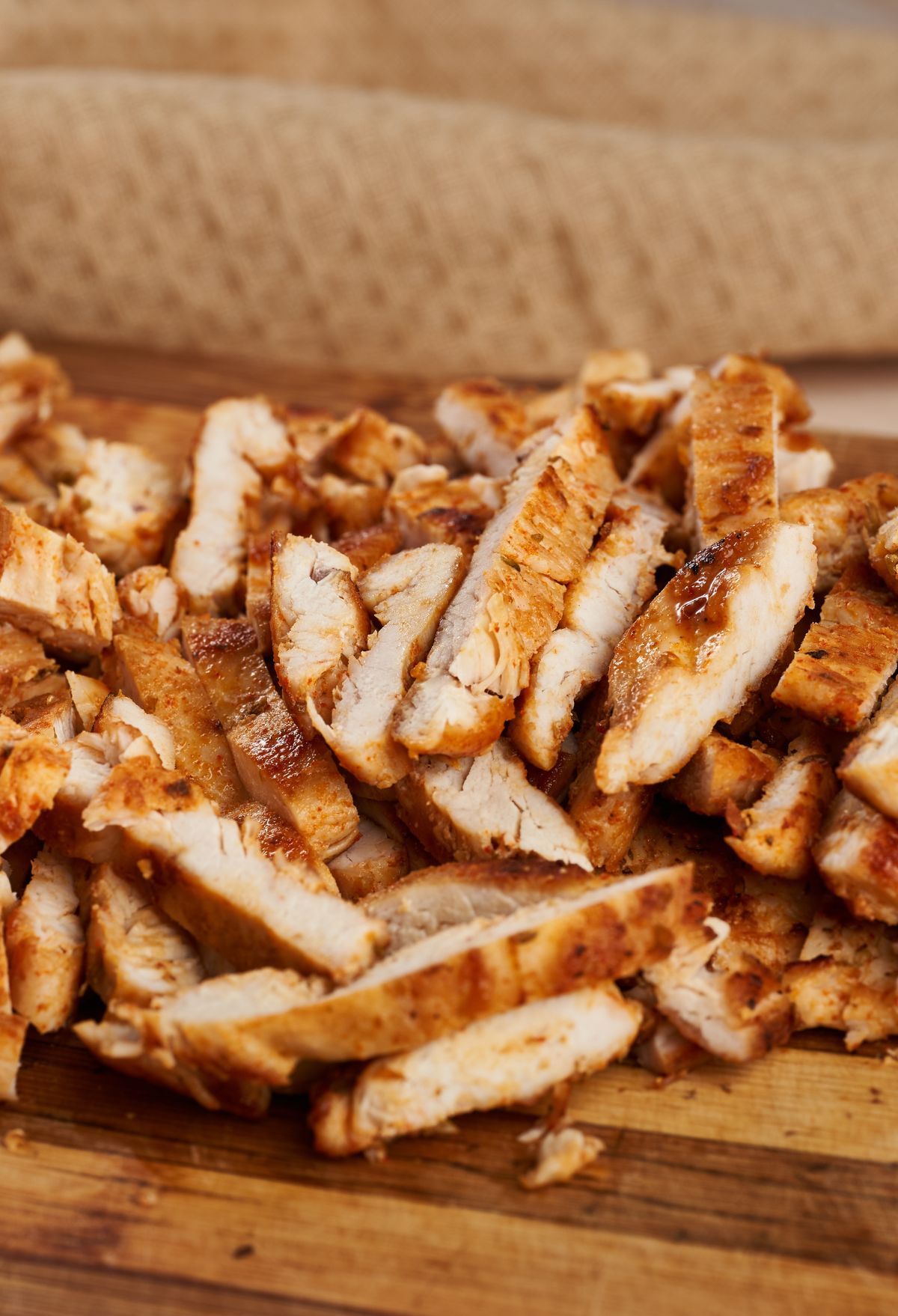 Sliced grilled chicken breast on a wooden cutting board.