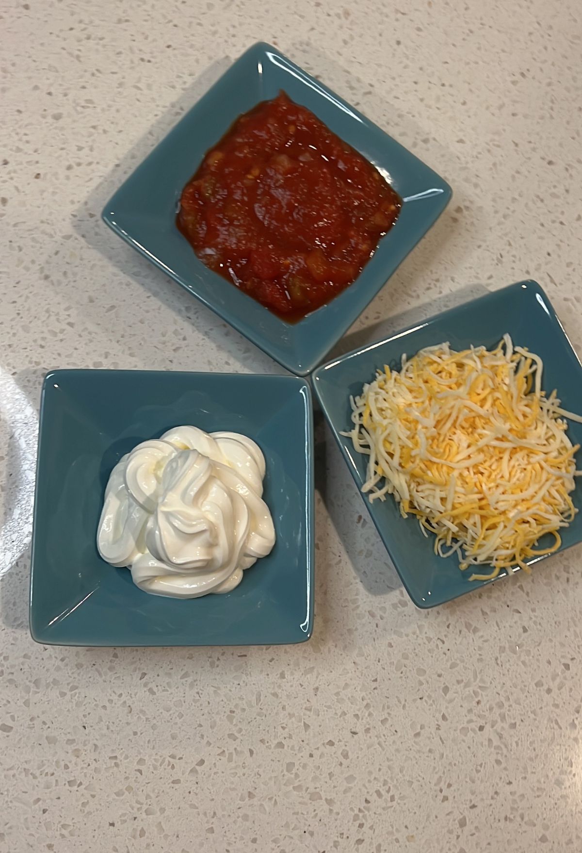 Three bowls with different food items: one with red salsa, one with sour cream, and one with shredded cheese.