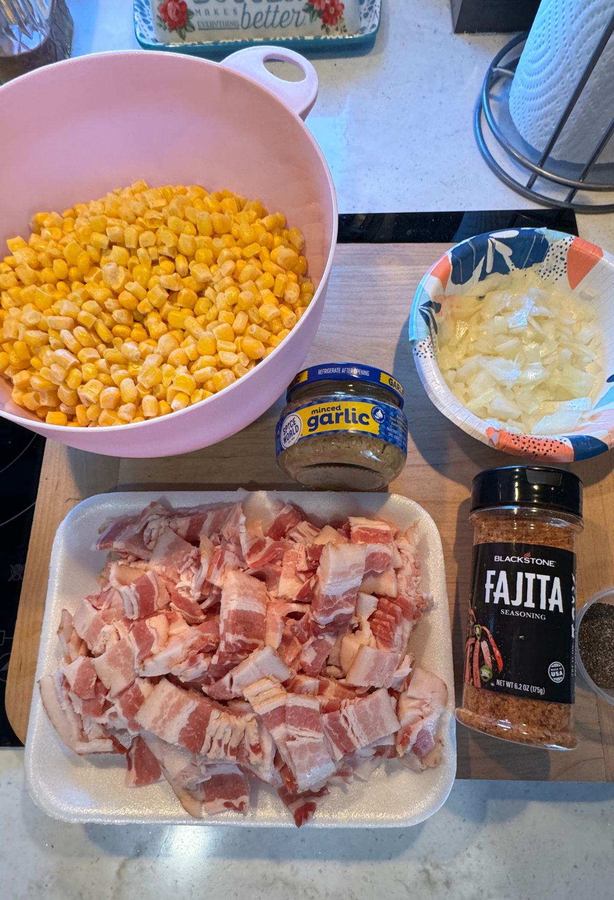 Ingredients for a meal preparation including diced bacon, corn, chopped onions, minced garlic, and fajita seasoning on a kitchen counter.