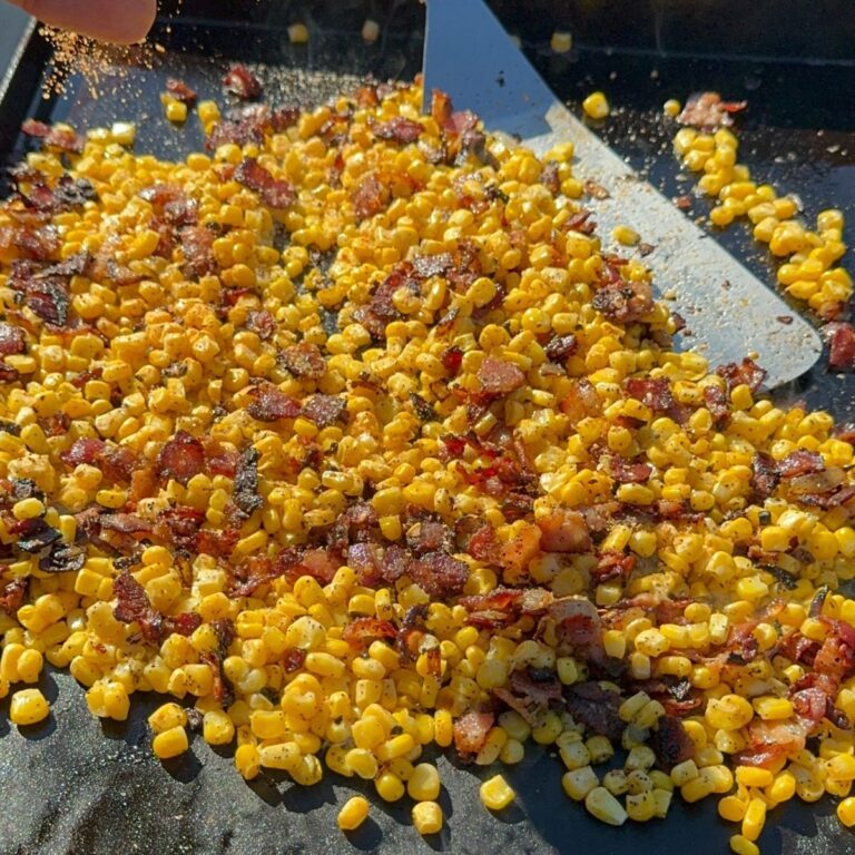 Corn and bacon bits being cooked on a flat grill.