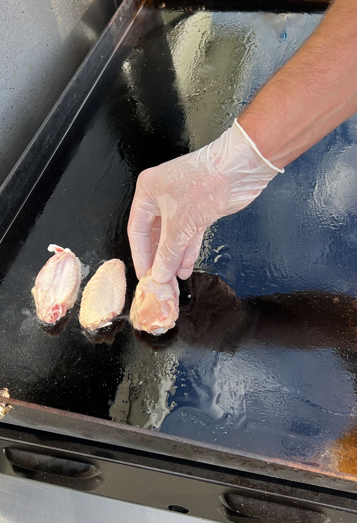 A person is putting chicken on a griddle.