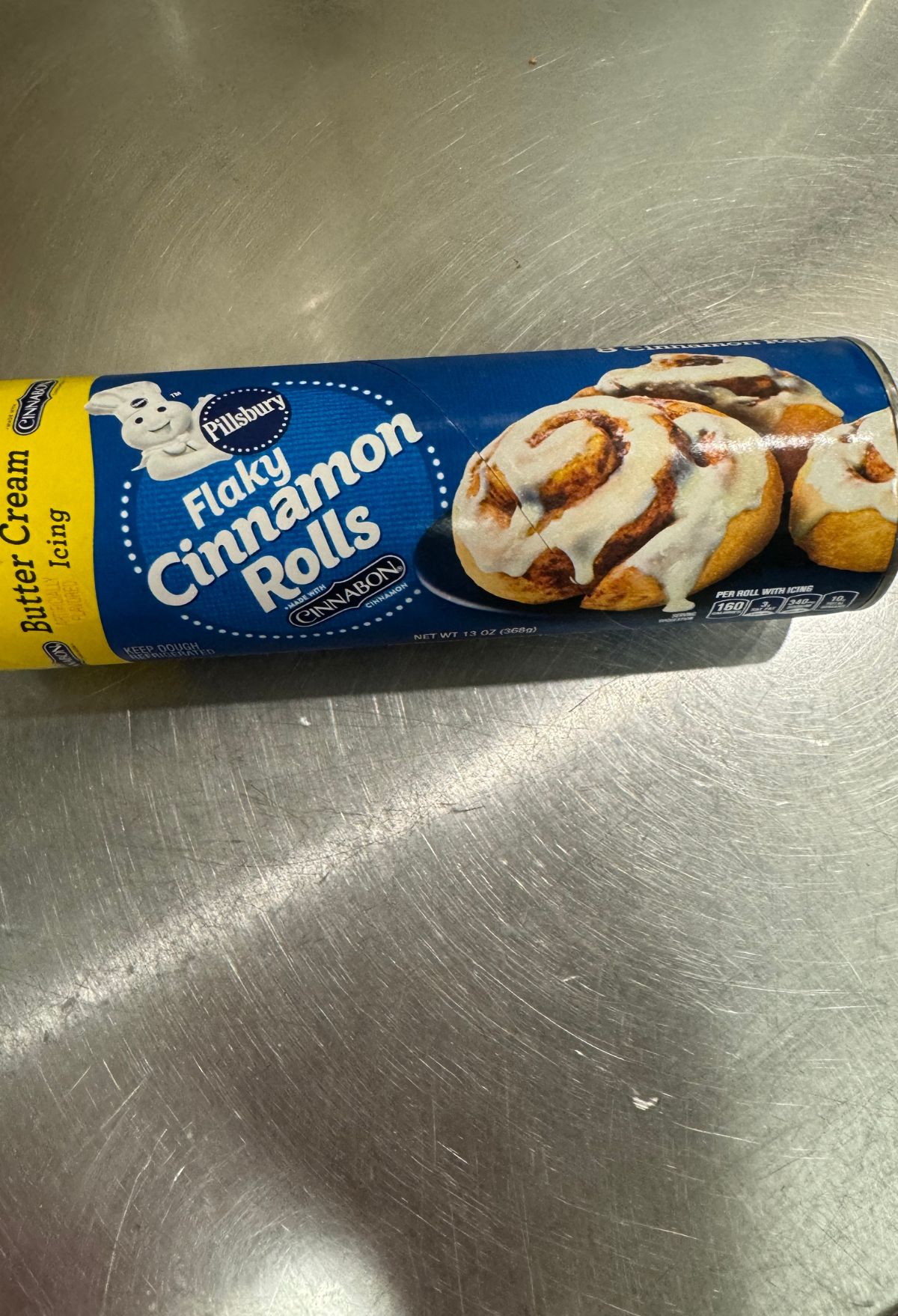 Package of pillsbury flaky cinnamon rolls with icing on a metal surface.