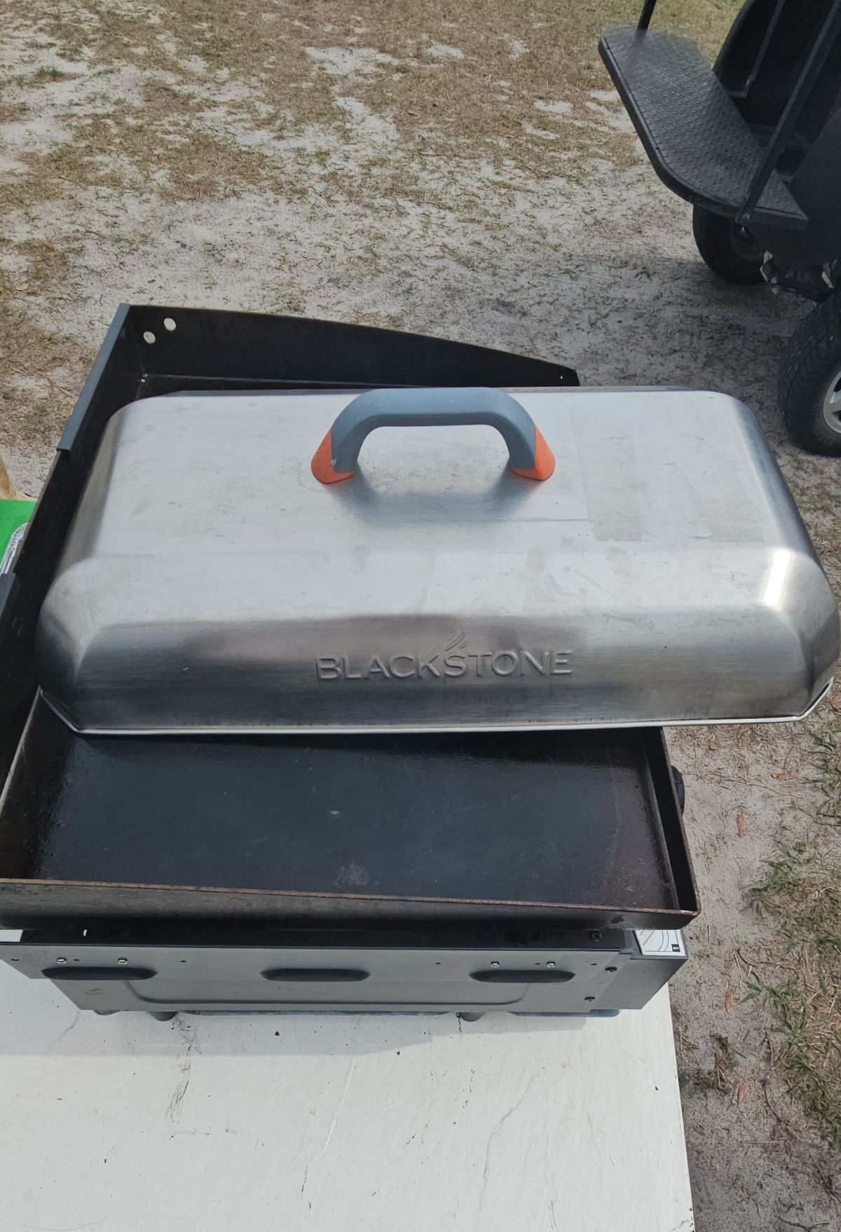 A blackstone griddle with an open lid, placed outdoors.