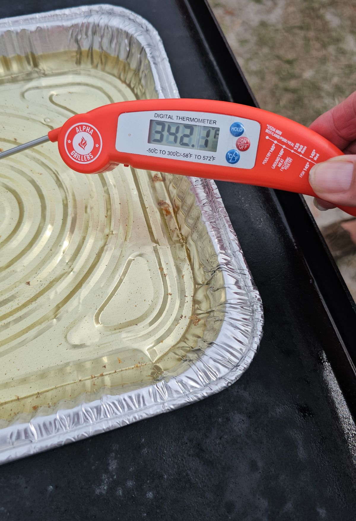 Person holding a digital thermometer displaying 392°f over an aluminum tray.