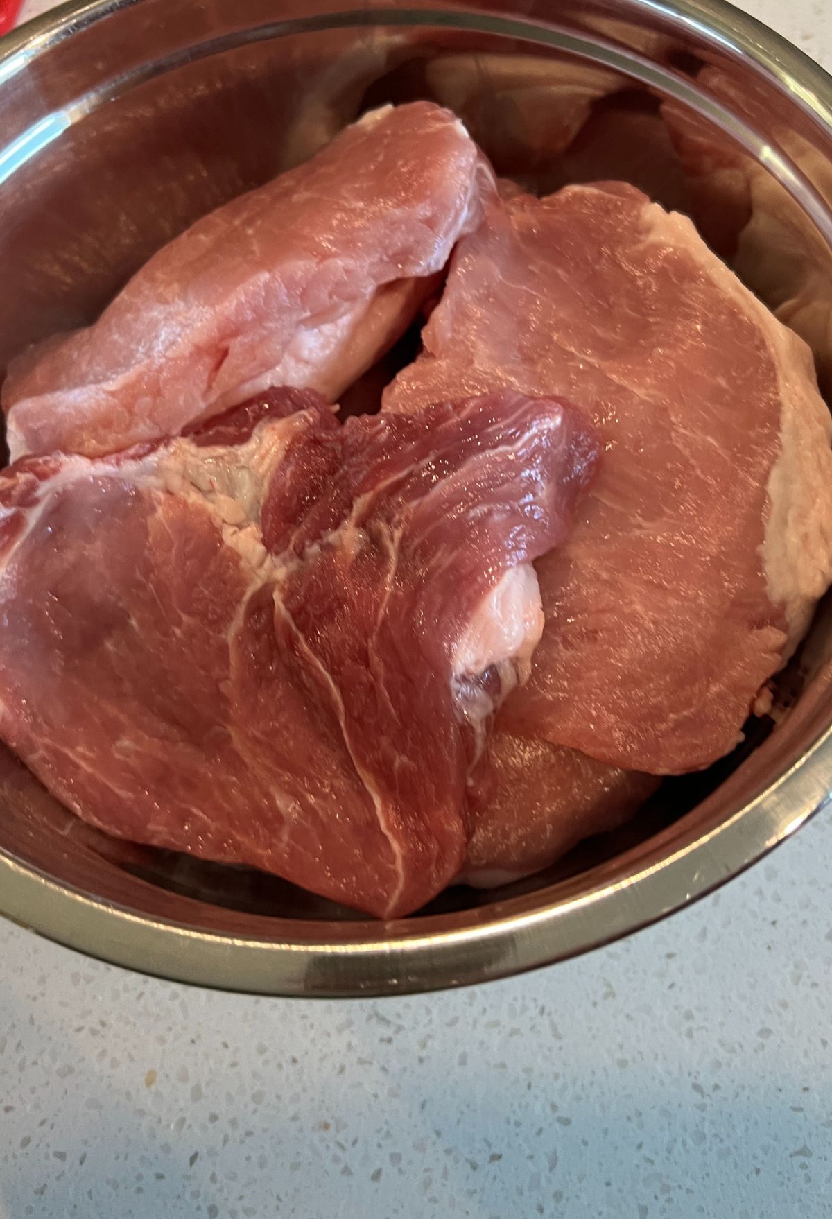 Raw pork chops in a stainless steel bowl.