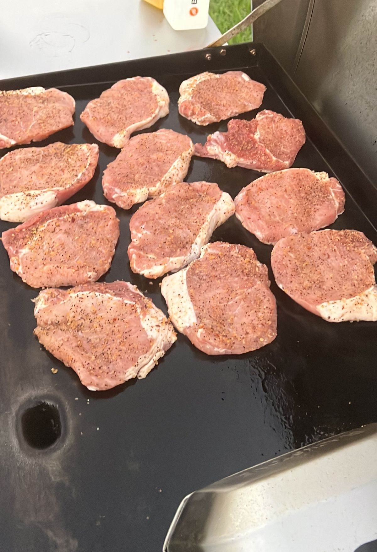 Several seasoned pork chops cooking on a flat grill.