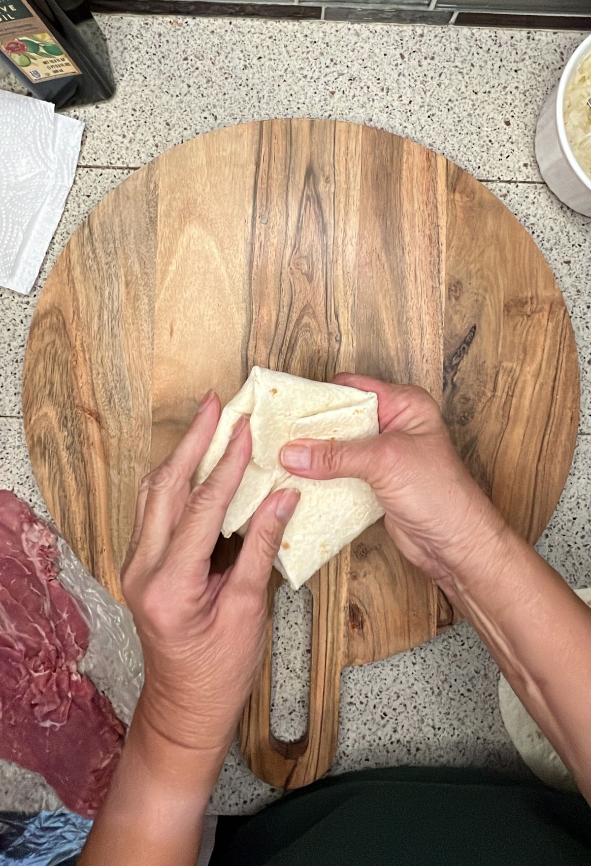 Person folding a tortilla on a wooden cutting board.