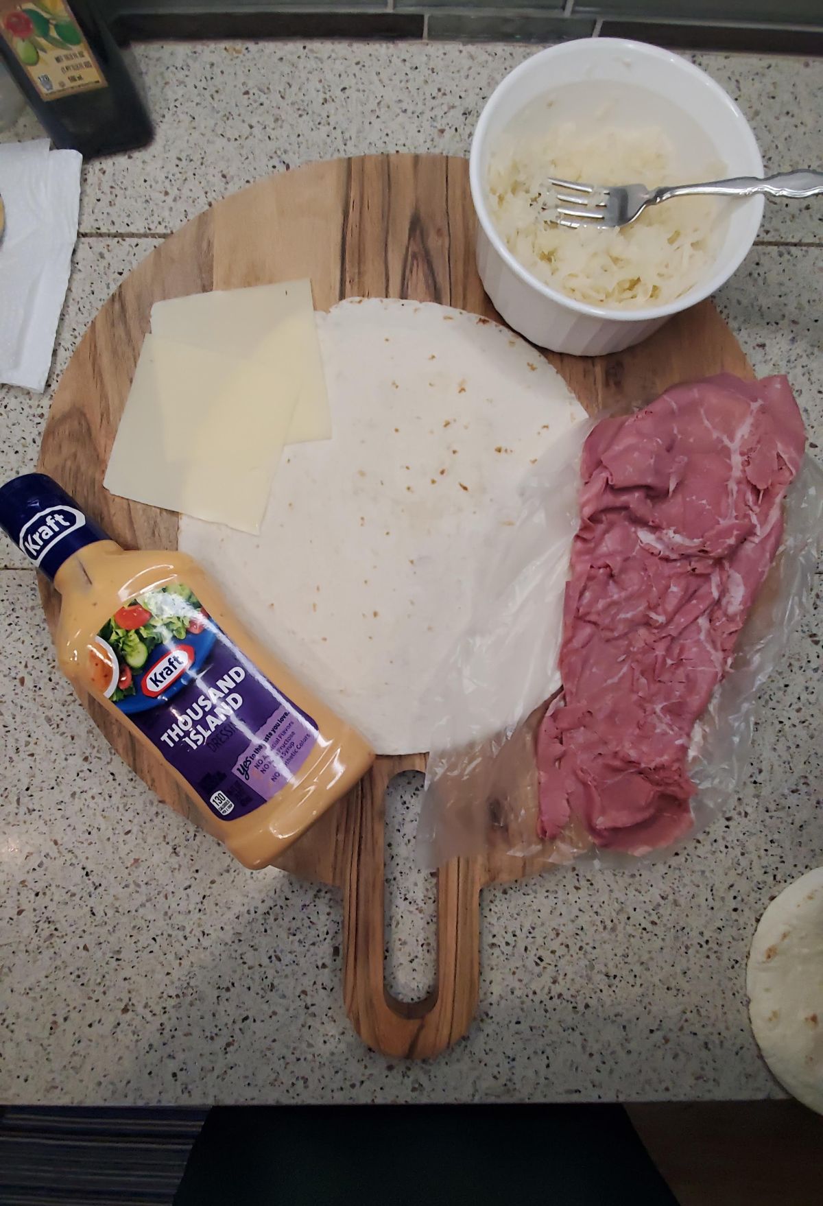 Ingredients for a sandwich laid out on a wooden cutting board, including roast beef, cheese slices, a tortilla, mayonnaise, and a side of coleslaw.