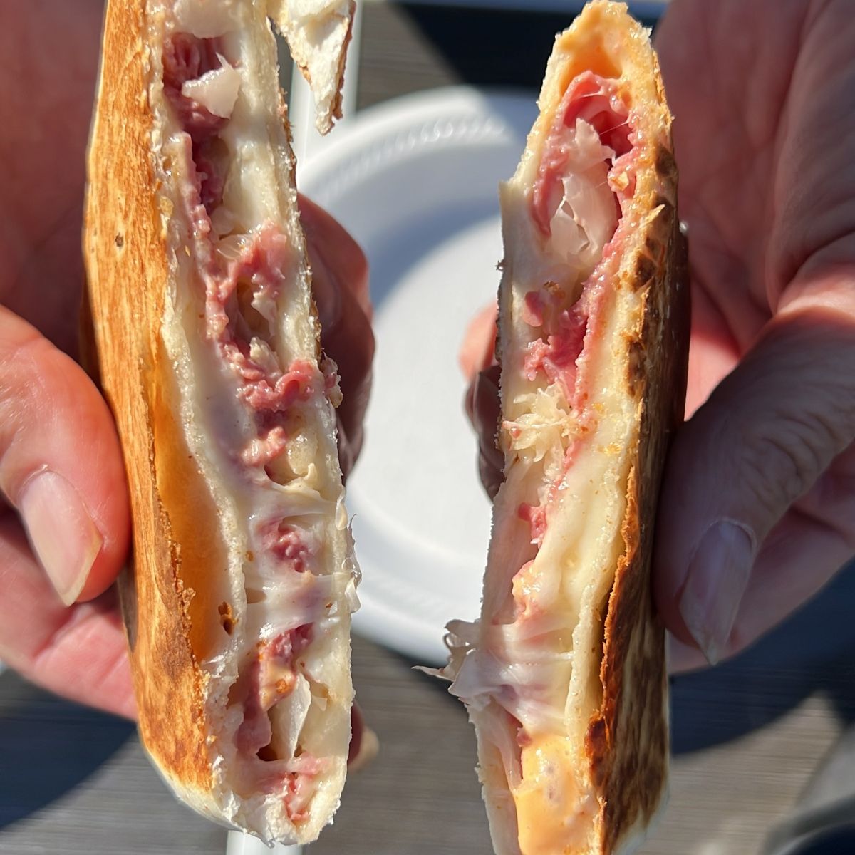 Two hands holding a halved toasted sandwich with melted cheese and ham.