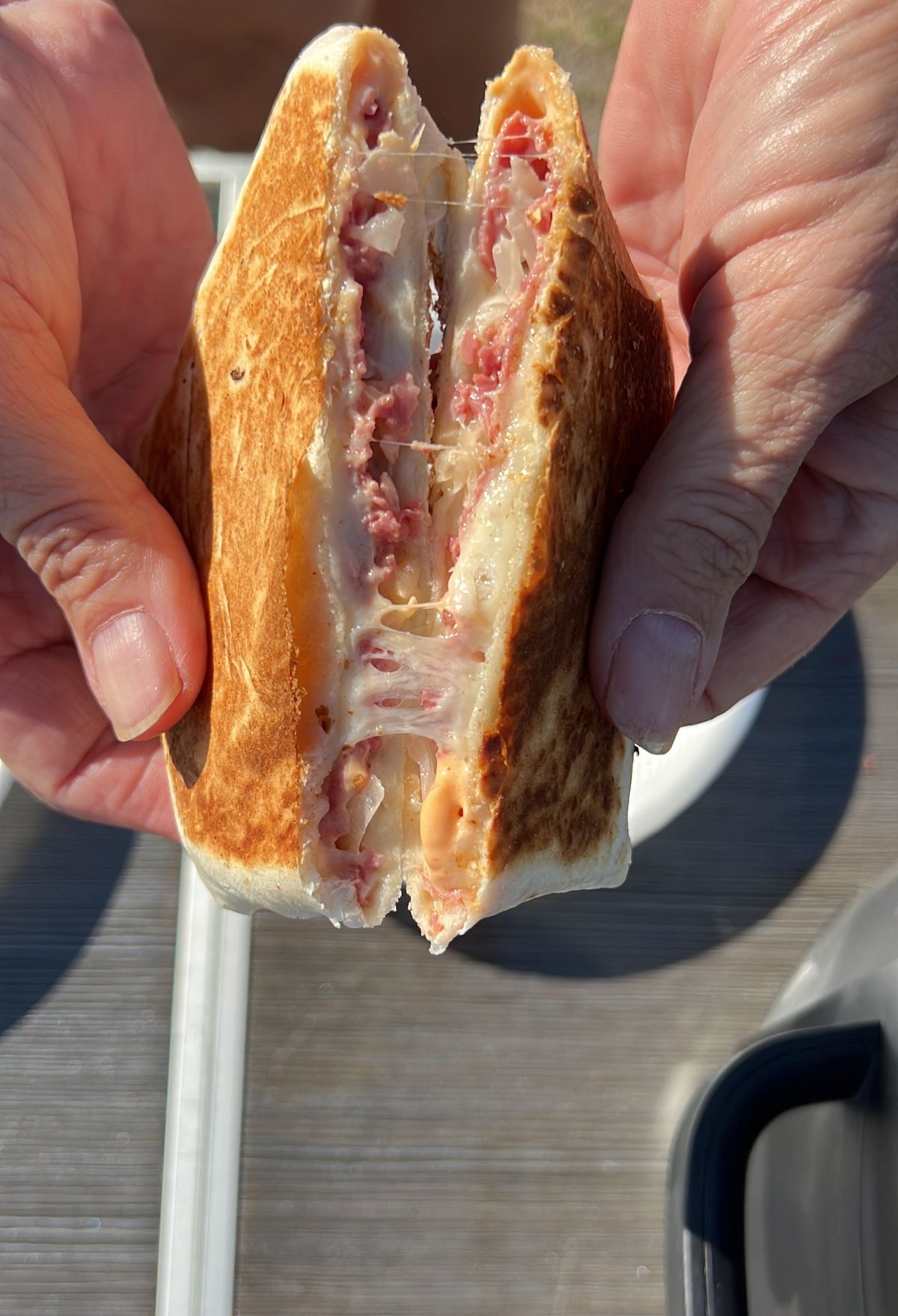 A person holding a toasted sandwich with melted cheese and meat filling.