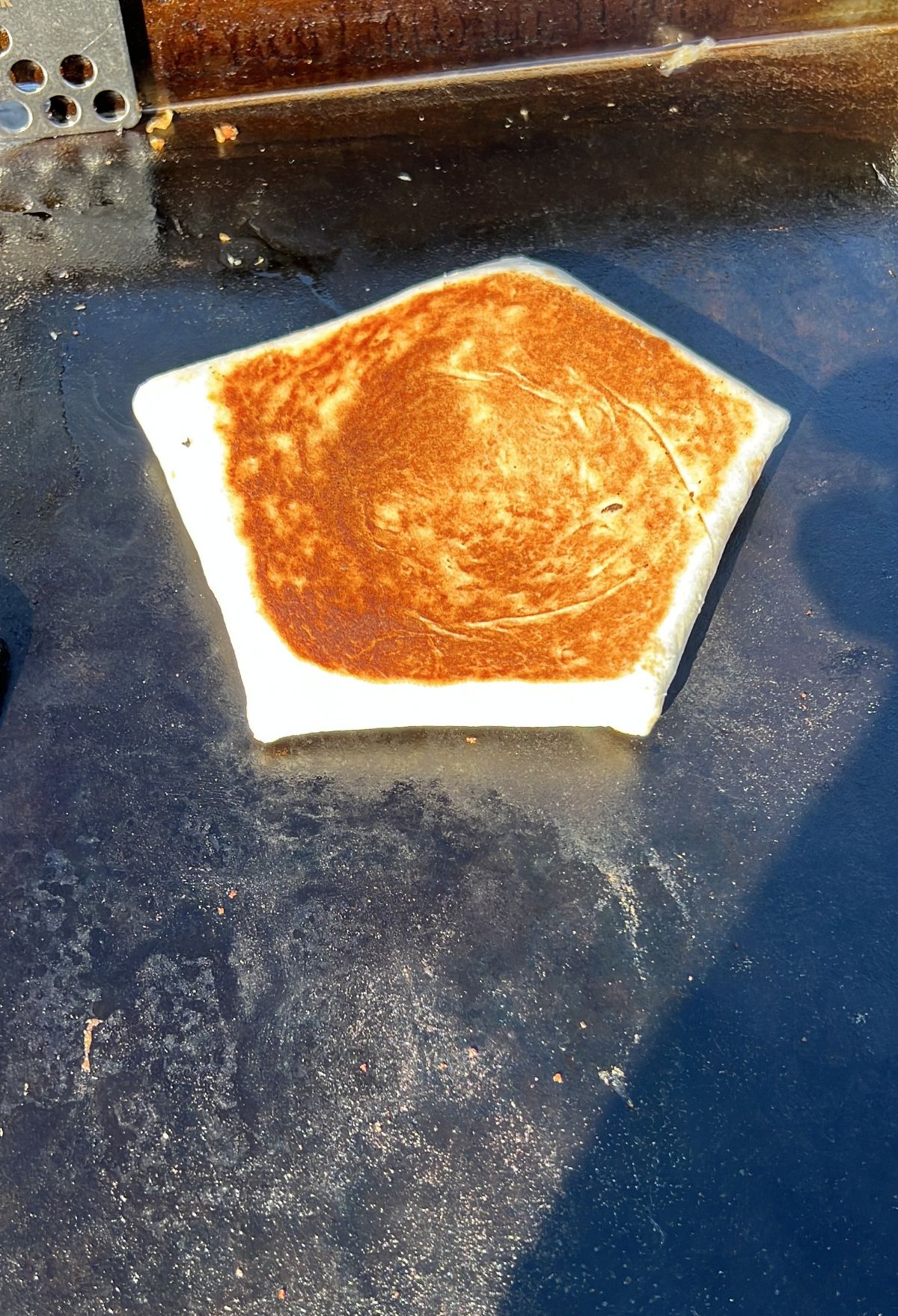 A pentagon-shaped bread toasting on a griddle.