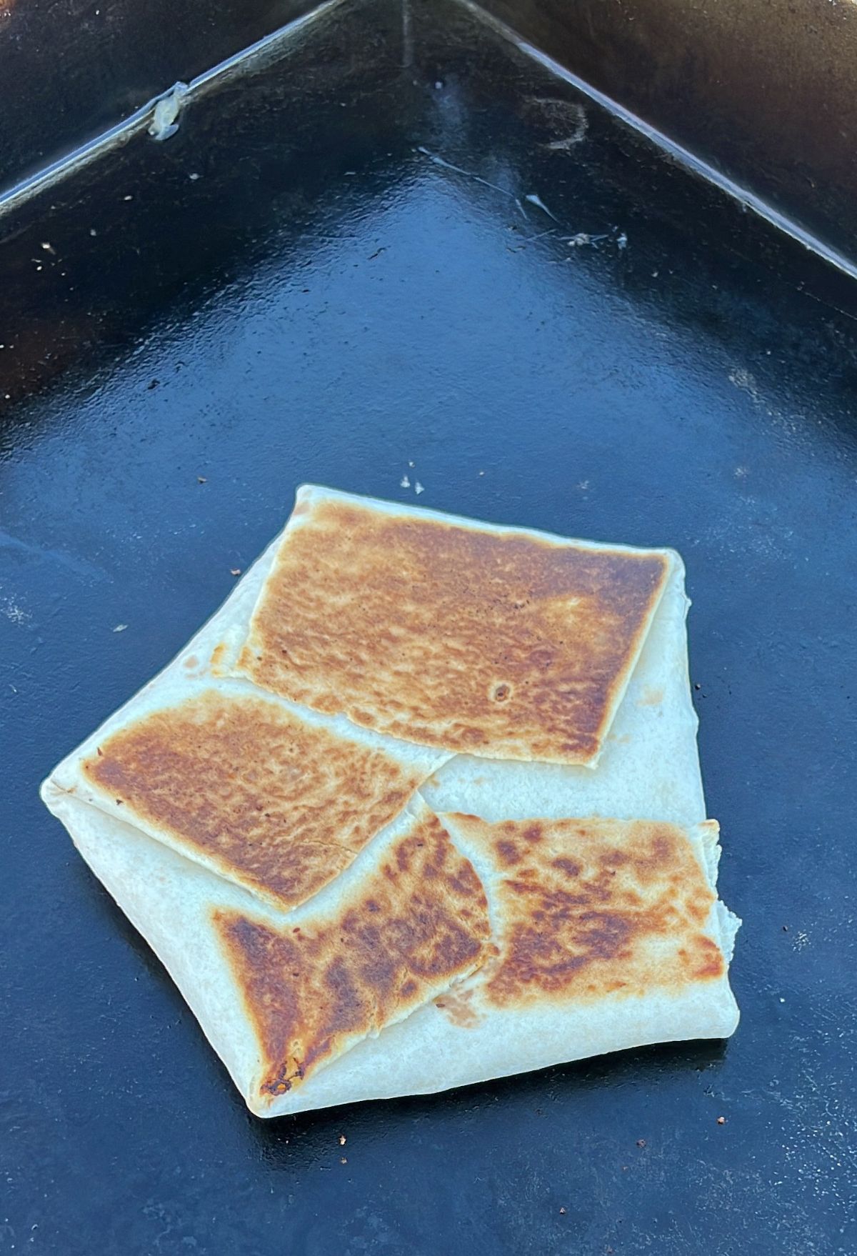 A folded and partially broken quesadilla with golden-brown toasted spots on a griddle.