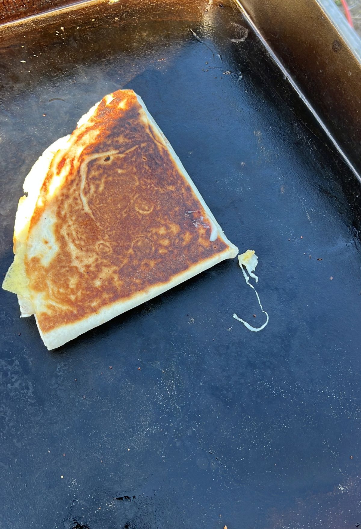 A golden-brown crepe folded on a cooking surface with some batter remnants.